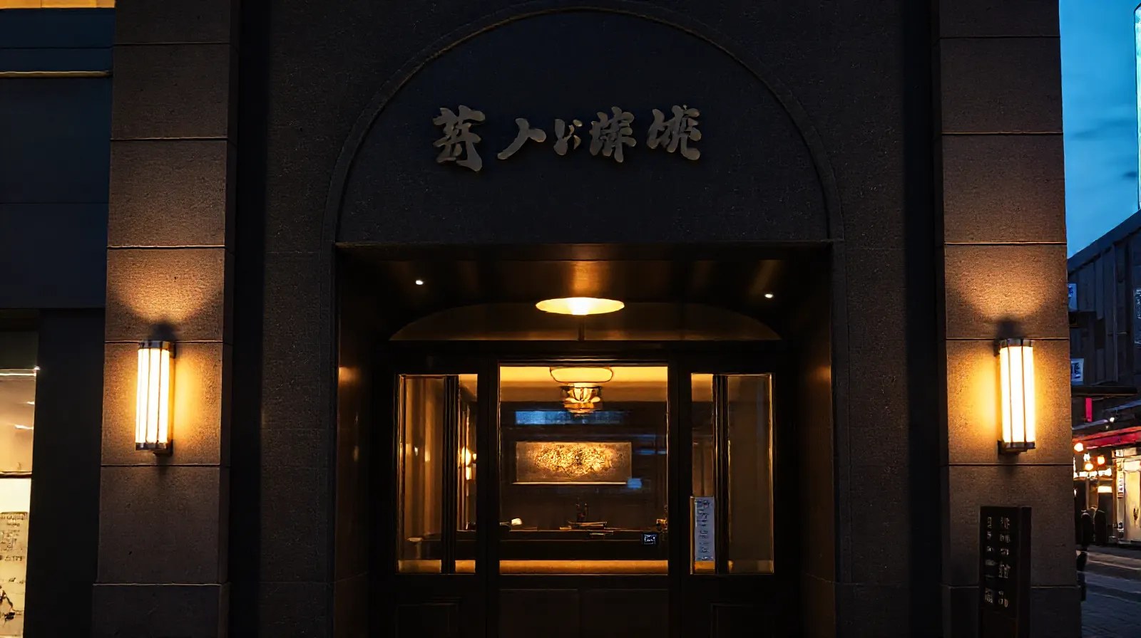 夕暮れの銀座、ダークストーンとブラスの灯りに照らされた高級店の入口